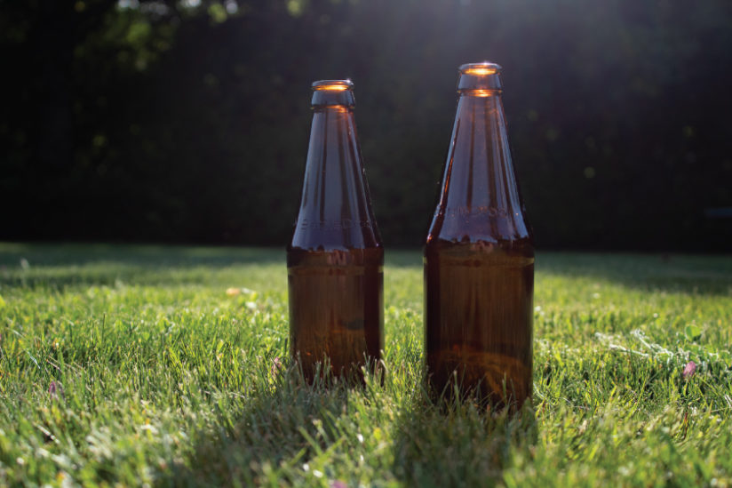 Two refillable glass bottles standing on a lawn.