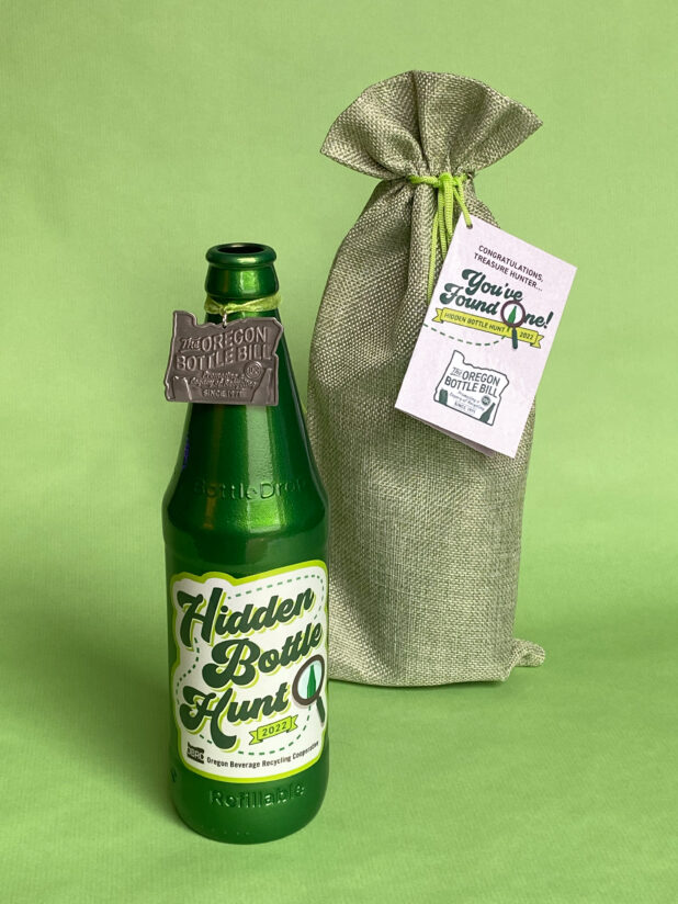 Green painted BottleDrop Refillable bottle standing next to a burlap bag with a green background. This one of the six bottles that will be hidden for our celebratory hidden bottle hunt to celebrate how Oregon's bottle bill has promoted recycling since 1971.